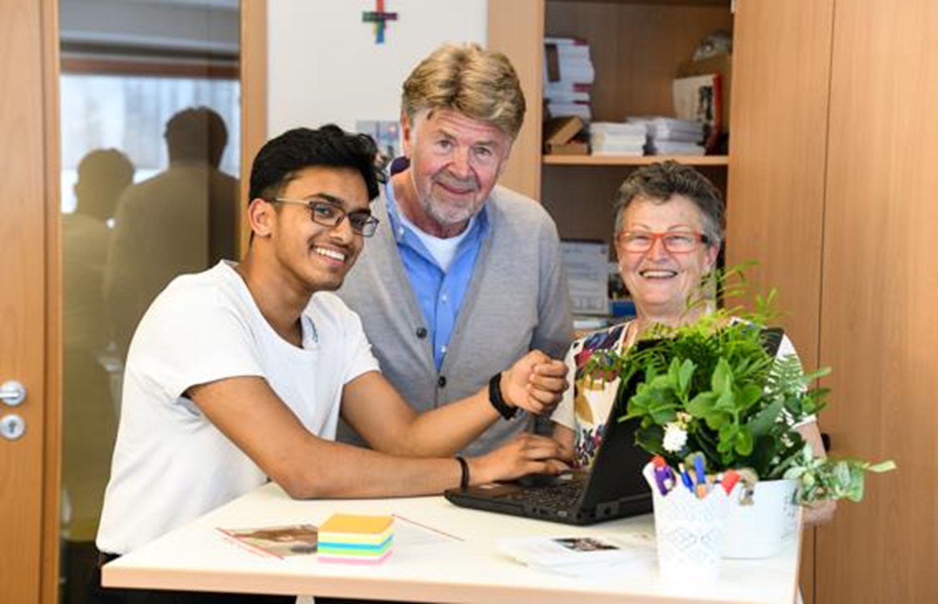 junger Mann mit Migrationshintergrund erklärt älterem Herrn und Frau Umgang mit dem PC